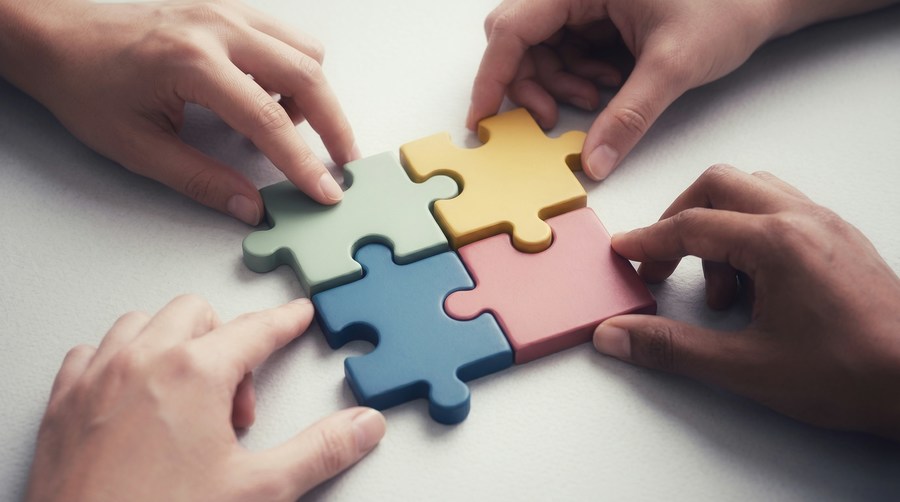 Vier handen maken samen een puzzel.